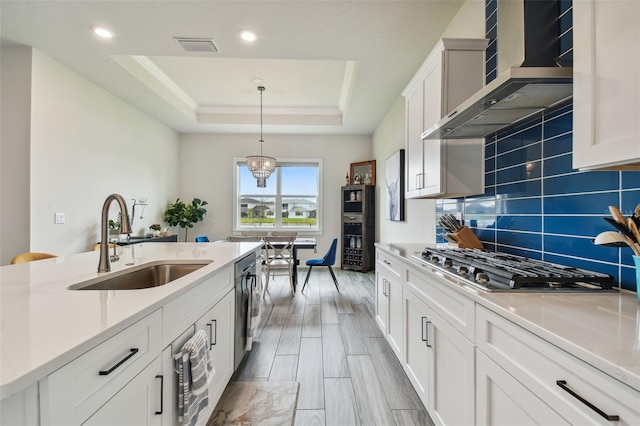 kitchen featuring a raised ceiling, sink, white cabinets, and wall chimney range hood