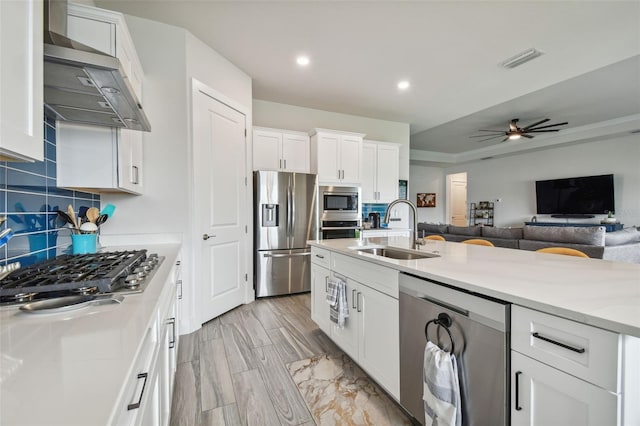 kitchen with decorative backsplash, stainless steel appliances, wall chimney range hood, sink, and white cabinets