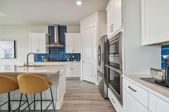 kitchen with a breakfast bar, sink, wall chimney exhaust hood, light wood-type flooring, and white cabinetry