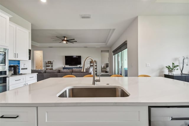 kitchen with a center island with sink, sink, ceiling fan, light stone countertops, and white cabinetry