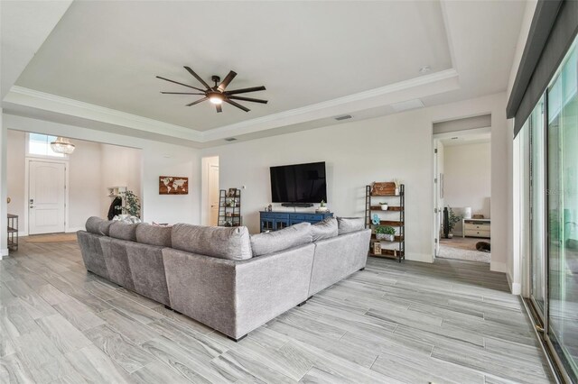 living room with a tray ceiling, ceiling fan, light hardwood / wood-style floors, and ornamental molding