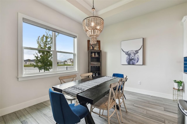 dining space with a raised ceiling, light wood-type flooring, and an inviting chandelier