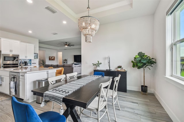 dining room with ceiling fan with notable chandelier, light wood-type flooring, a wealth of natural light, and a tray ceiling