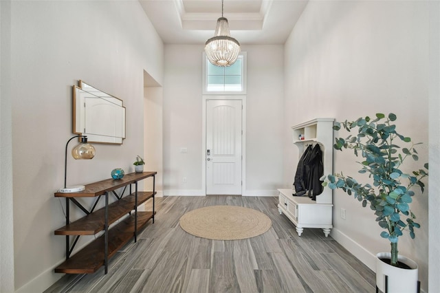 foyer entrance featuring light wood-type flooring, an inviting chandelier, and a raised ceiling