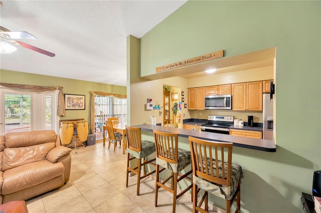 kitchen with appliances with stainless steel finishes, light tile patterned flooring, kitchen peninsula, a kitchen breakfast bar, and ceiling fan