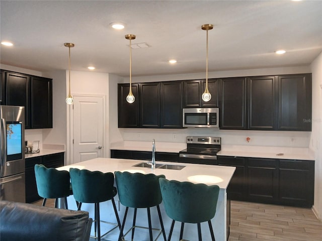 kitchen featuring sink, light wood-type flooring, stainless steel appliances, pendant lighting, and a kitchen island with sink