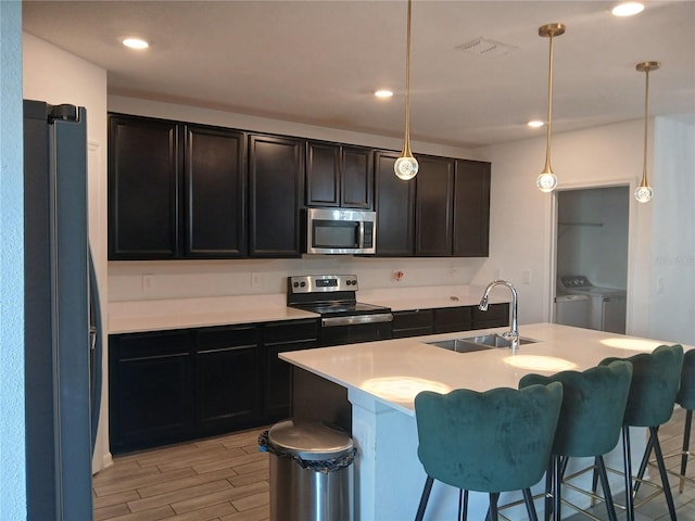 kitchen featuring light hardwood / wood-style flooring, stainless steel appliances, sink, washing machine and dryer, and decorative light fixtures