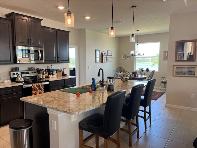 kitchen with a breakfast bar area, an island with sink, hanging light fixtures, stainless steel appliances, and a textured ceiling