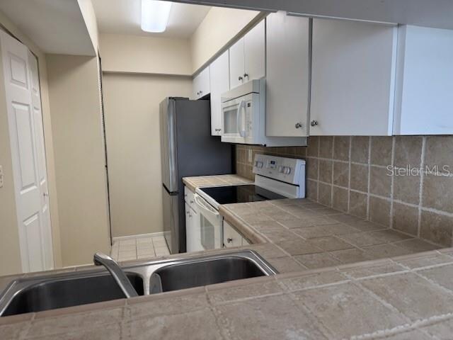 kitchen featuring white appliances, sink, tile counters, white cabinets, and decorative backsplash