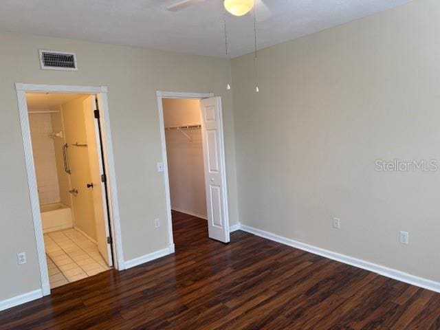 unfurnished bedroom featuring ensuite bathroom, a walk in closet, a closet, ceiling fan, and dark wood-type flooring