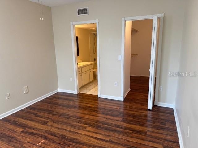 unfurnished bedroom with dark wood-type flooring, a walk in closet, and ensuite bath