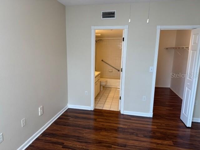 unfurnished bedroom featuring a walk in closet, dark hardwood / wood-style floors, a closet, and ensuite bath