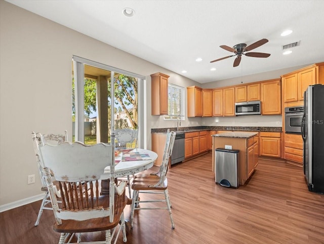 kitchen with light hardwood / wood-style floors, appliances with stainless steel finishes, a kitchen island, and ceiling fan