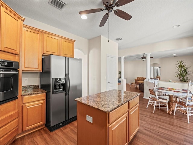 kitchen featuring a center island, ornate columns, black oven, hardwood / wood-style flooring, and stainless steel refrigerator with ice dispenser