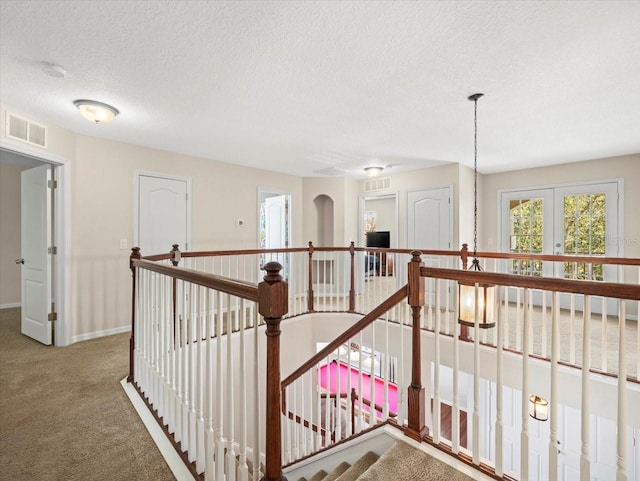 corridor with a textured ceiling, carpet flooring, and french doors