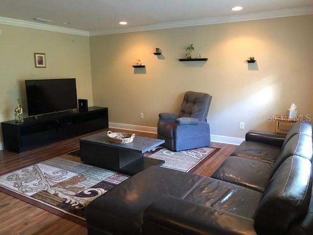living room featuring wood finished floors, baseboards, ornamental molding, and recessed lighting