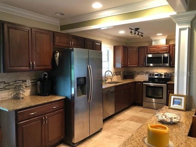 kitchen featuring a sink, stainless steel appliances, ornate columns, crown molding, and decorative backsplash