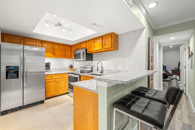 kitchen with ornamental molding, appliances with stainless steel finishes, tasteful backsplash, a kitchen bar, and kitchen peninsula