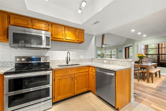 kitchen with sink, decorative backsplash, light stone countertops, kitchen peninsula, and stainless steel appliances