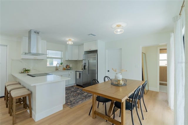 kitchen featuring white cabinetry, light hardwood / wood-style floors, stainless steel appliances, wall chimney exhaust hood, and decorative backsplash