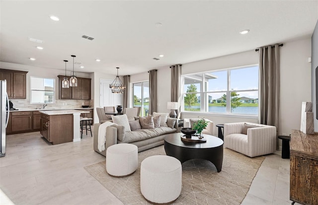 living room featuring an inviting chandelier, plenty of natural light, sink, and a water view