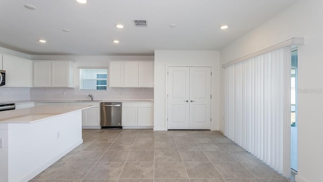 kitchen with sink, dishwasher, white cabinetry, light tile patterned flooring, and decorative backsplash