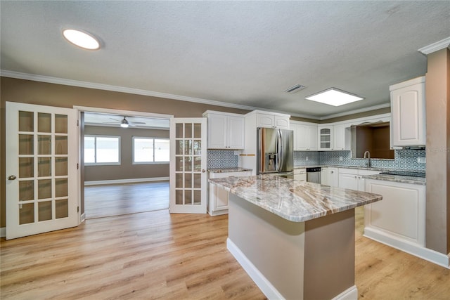 kitchen with white cabinets, light stone counters, light hardwood / wood-style flooring, stainless steel appliances, and a center island