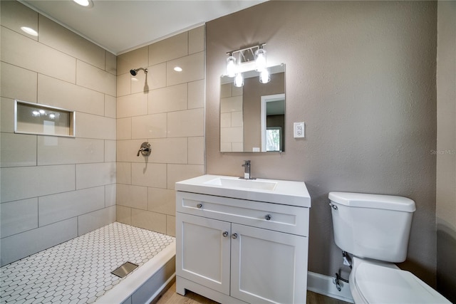 bathroom with toilet, vanity, and tiled shower