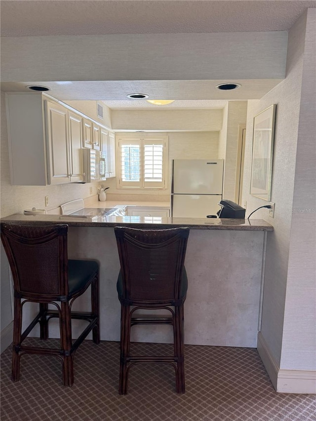 kitchen featuring a breakfast bar, kitchen peninsula, and white refrigerator