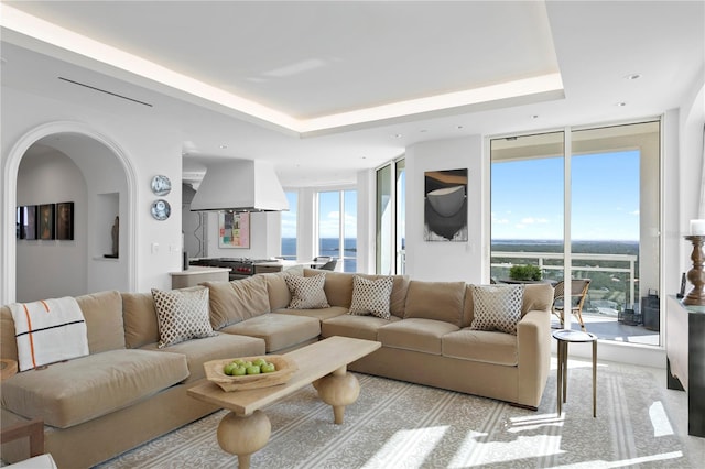 living room with a water view, expansive windows, and a tray ceiling