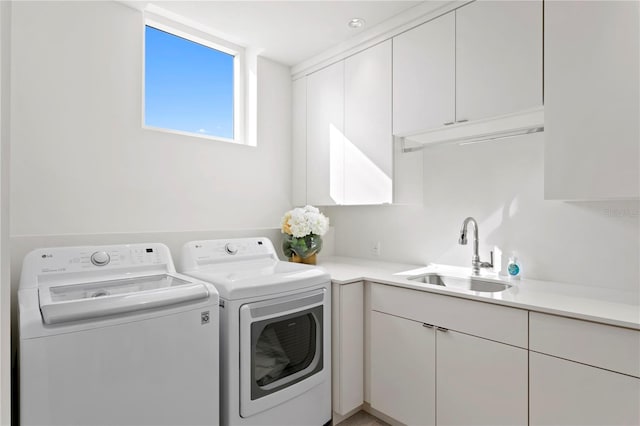 clothes washing area featuring sink, washing machine and clothes dryer, and cabinets