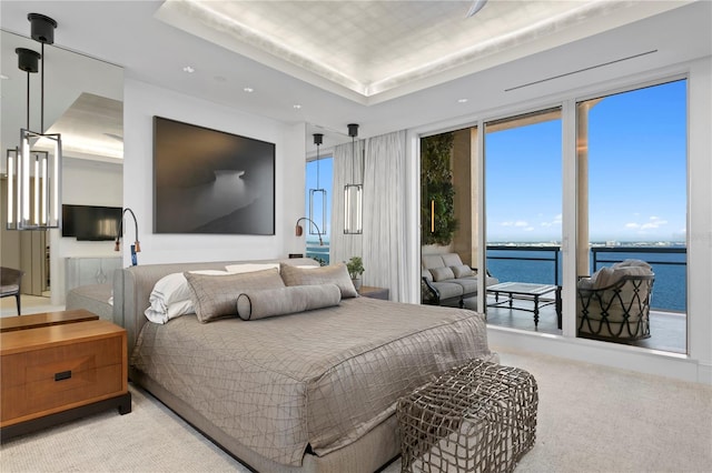 bedroom featuring a water view, light carpet, a raised ceiling, and access to exterior