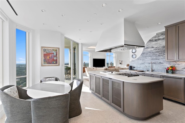 kitchen with a kitchen island, backsplash, sink, dark brown cabinetry, and stainless steel gas stovetop