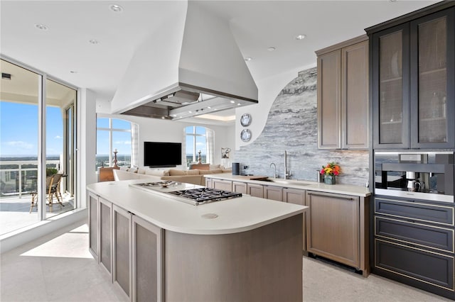 kitchen with island exhaust hood, backsplash, stainless steel gas stovetop, sink, and a center island