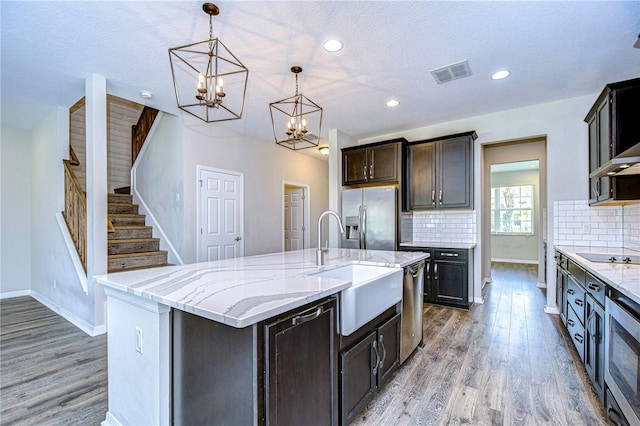 kitchen with hardwood / wood-style floors, a center island with sink, appliances with stainless steel finishes, a textured ceiling, and pendant lighting