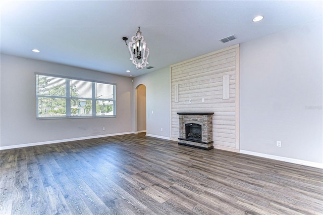 unfurnished living room featuring a stone fireplace, a notable chandelier, and hardwood / wood-style floors