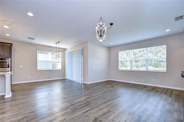 unfurnished living room with dark wood-type flooring, a healthy amount of sunlight, and a chandelier