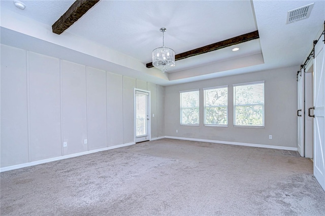 empty room featuring carpet floors, a tray ceiling, a barn door, a notable chandelier, and a textured ceiling