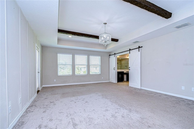 interior space with connected bathroom, light carpet, a raised ceiling, and a barn door