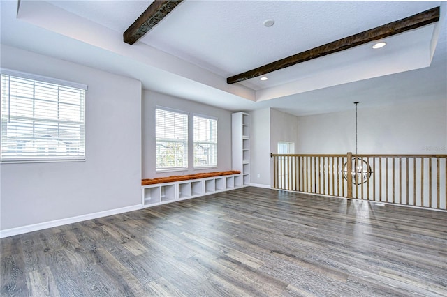 empty room featuring beam ceiling, wood-type flooring, a wealth of natural light, and a chandelier