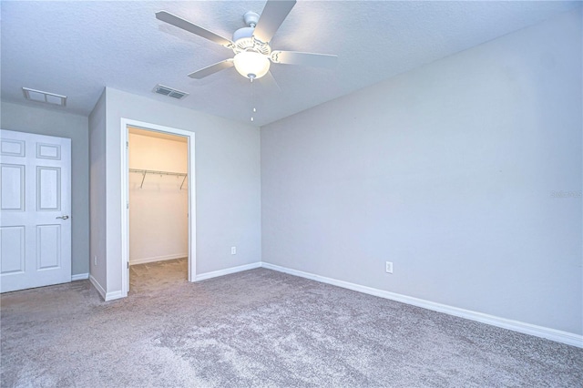 unfurnished bedroom with carpet floors, a closet, a spacious closet, a textured ceiling, and ceiling fan