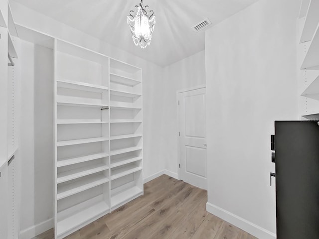 walk in closet featuring light hardwood / wood-style flooring and a chandelier