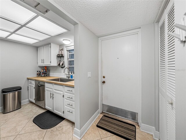 kitchen with stainless steel dishwasher, white cabinetry, sink, and butcher block countertops