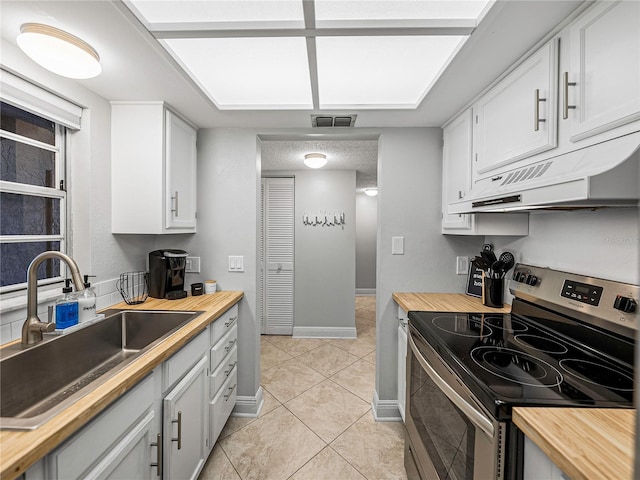 kitchen featuring stainless steel electric range, white cabinets, light tile patterned floors, sink, and premium range hood