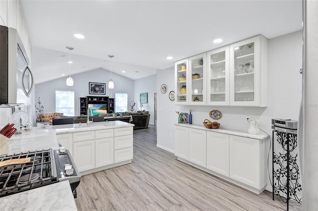 kitchen with white cabinets, light stone countertops, vaulted ceiling, light hardwood / wood-style flooring, and black range