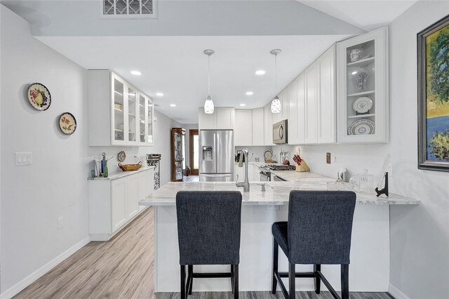 kitchen featuring light hardwood / wood-style flooring, kitchen peninsula, white cabinets, a kitchen bar, and appliances with stainless steel finishes