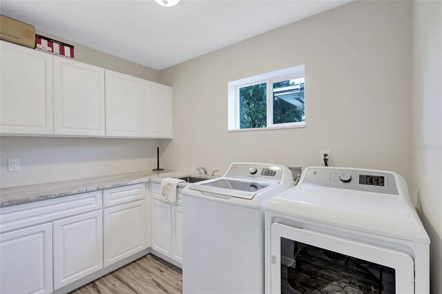 washroom featuring sink, light hardwood / wood-style flooring, washing machine and clothes dryer, and cabinets