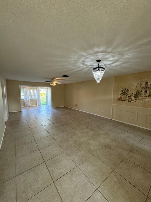 empty room featuring ceiling fan with notable chandelier, a textured ceiling, and light tile patterned flooring