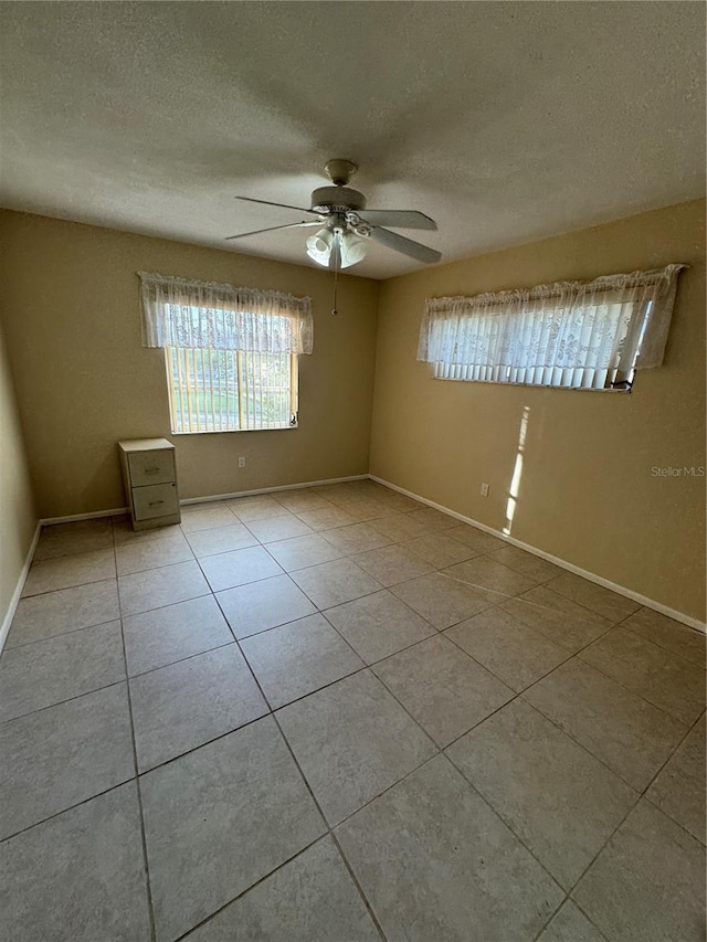 spare room with a textured ceiling, light tile patterned floors, and ceiling fan