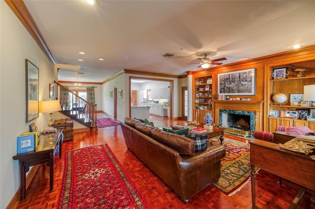 living room featuring a high end fireplace, dark parquet flooring, ceiling fan with notable chandelier, built in features, and crown molding